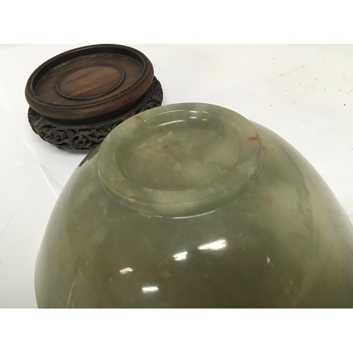 1041 - A 19th century Chinese green jade bowl with a carved hardwood stand. The bowl with stress cracks pos... 