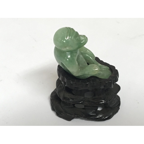 1046 - A small Chinese carved green jade monkey on a hardwood base. Height including stand 5cm