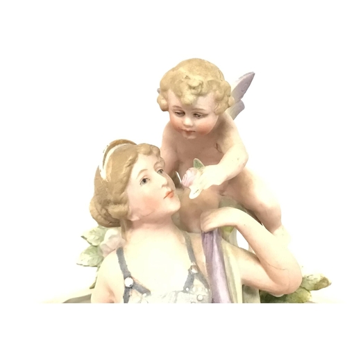 1104 - Bisque European figure group depicting a woman & Putto, 25cm tall. Postage cat D