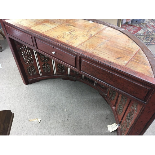 1702 - An Indonesian desk of semi circular shape the top supported by carved vertical supports with a drawe... 