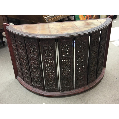 1702 - An Indonesian desk of semi circular shape the top supported by carved vertical supports with a drawe... 