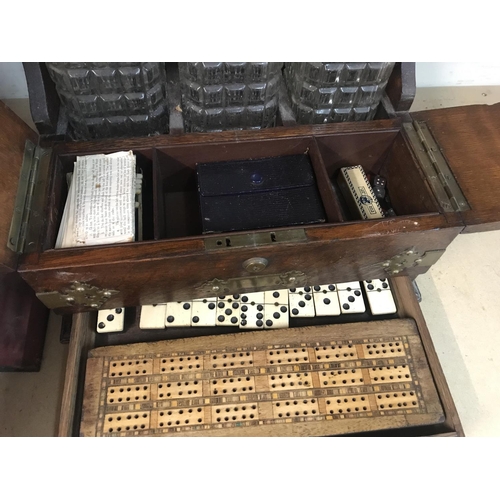 1334 - A oak Tantalus inset with three decanters together with domino's and cribbage board.