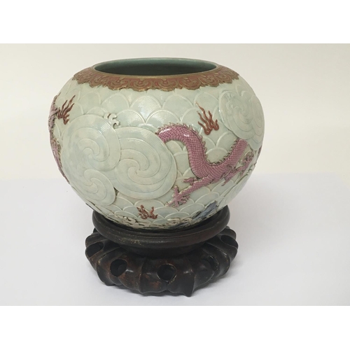 1039 - An unusual raised relief Chinese pot on a hardwood stand with pink dragons and a raised cloud patter... 