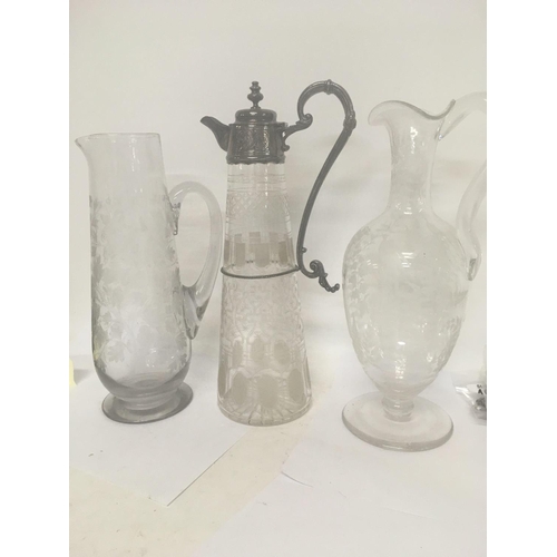 1290 - A glass claret jug with silver plated mounts and etched sides and two other etched jugs .