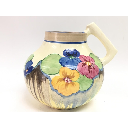 926 - A clarice cliff hand painted pansies pattern jug with an unsual shape. 19cm tall.Slight chip seen on... 