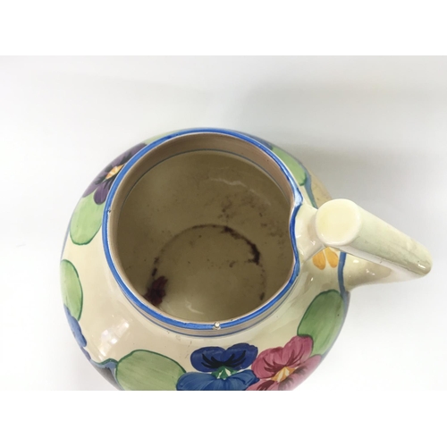 926 - A clarice cliff hand painted pansies pattern jug with an unsual shape. 19cm tall.Slight chip seen on... 