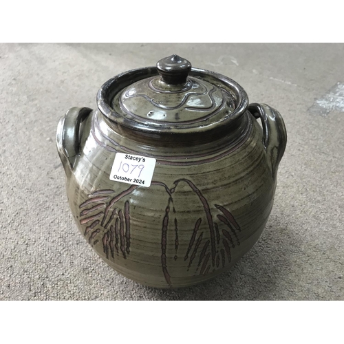 1079 - A jar and cover with raised side handles, dark green glaze incised decoration and impressed potters ... 