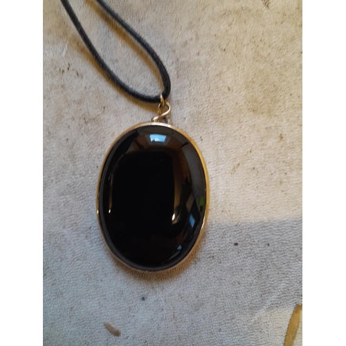 143 - Black hardstone set in clearly hallmarked 9 ct gold pendant on leather thong 14 g