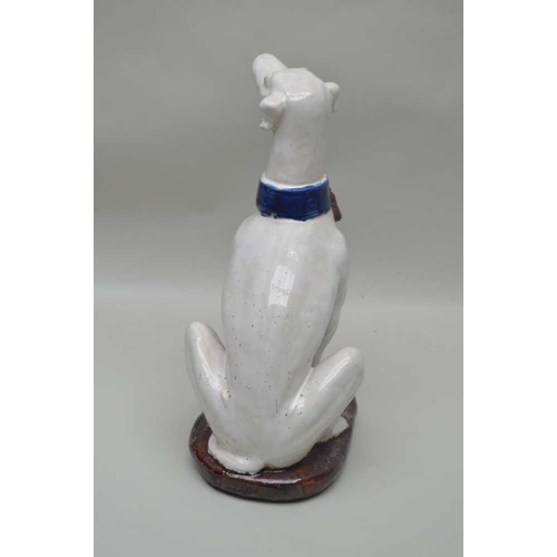 115 - A CONTINENTAL GLAZED POTTERY FIGURINE OF A SEATED LONG DOG with tasselled collar, 35.5cm high 