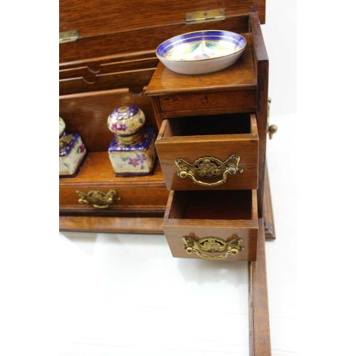 308 - AN EDWARDIAN OAK WRITING CABINET with drop fronted glass panel, revealing drawers and two inkwells, ... 