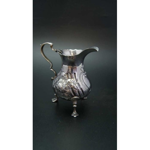 78 - John Muns, a George III silver cream jug, embossed floral decoration, raised on three trefid support... 