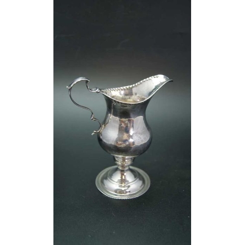 16 - A George III silver cream jug of baluster form with punched rim, C scroll handle and raised circular... 