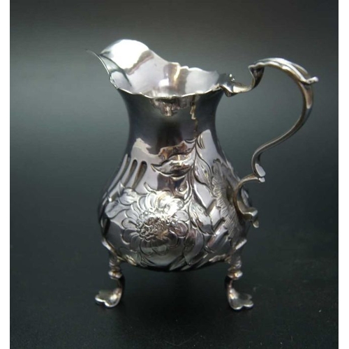 18 - John Muns, a George III silver cream jug, embossed floral decoration, raised on three trefid support... 