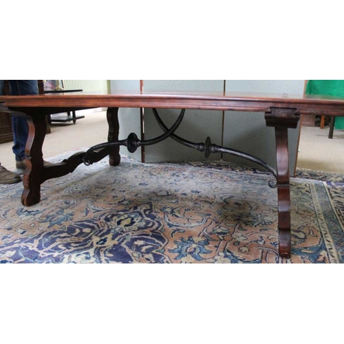 212 - An imported hardwood low coffee table in a Spanish style with cast iron stretcher, 50cm x 148cm x 97... 