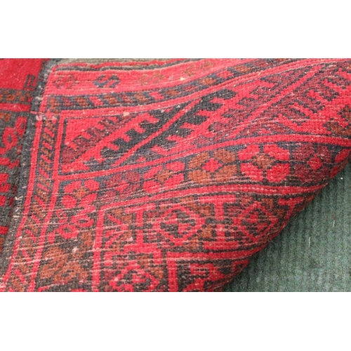 176 - A large sized woven woolen floor carpet of red ground, with multiple central elephants feet, within ... 