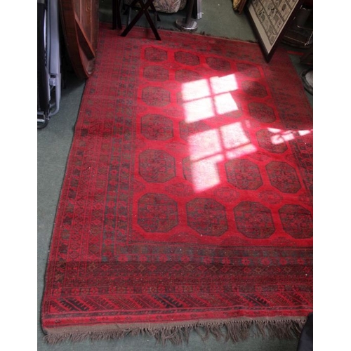 176 - A large sized woven woolen floor carpet of red ground, with multiple central elephants feet, within ... 