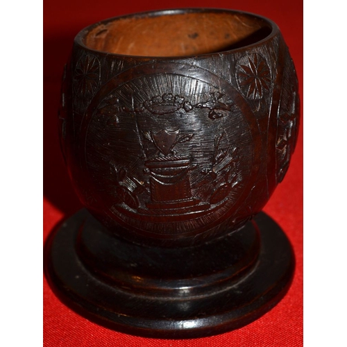 12 - A 19th century coconut cup carved with trophies of music and war on a -platform base 10 cm high