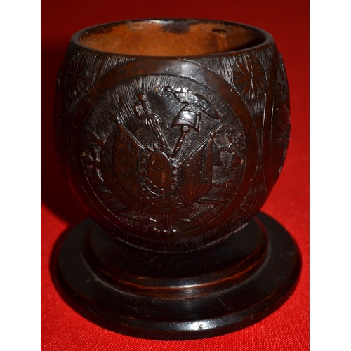 12 - A 19th century coconut cup carved with trophies of music and war on a -platform base 10 cm high