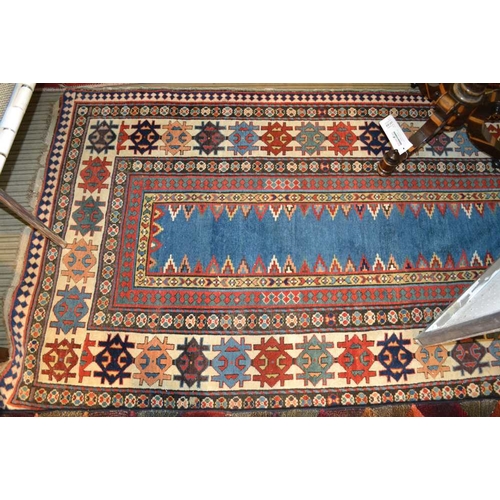 96 - An antique Kazak long rug, having narrow plain central blue panel, within a framework of borders in ... 