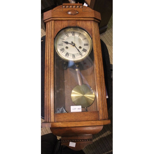 208 - An oak cased wall clock, the glazed door reveals dial with Roman numerals & drop pendulum