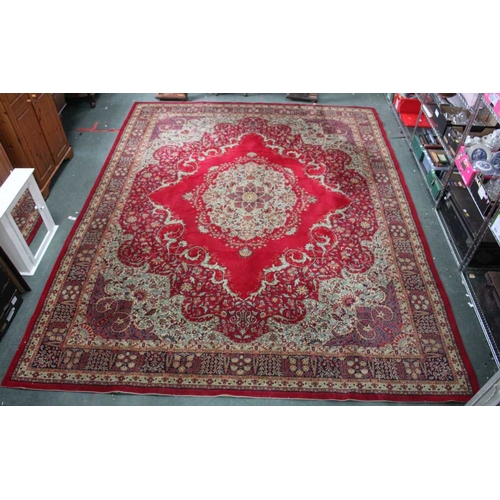 58 - A large machine made Persian design carpet, crimson ground with central floral motif, having scrolli... 