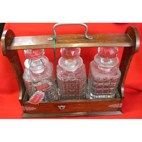 427 - An oak framed tantalus, contains three cut glass spirit decanters, together with two silver labels