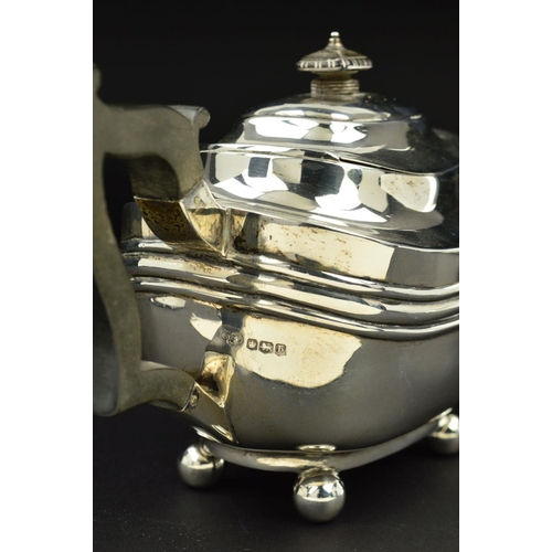 109 - A GEORGE V SILVER BACHELOR'S TEAPOT, of shaped rectangular form, ebonised fitments and on four ball ... 