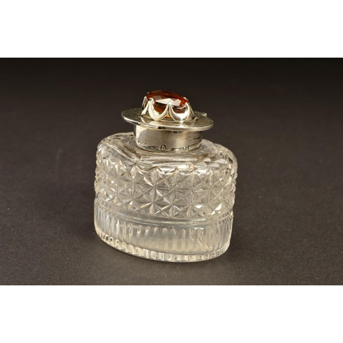 194 - AN EDWARDIAN SILVER MOUNTED OVAL GLASS INKWELL, the hinged cover set with a Cairngorm (brown quartz)... 