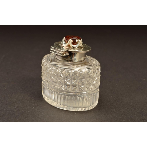 194 - AN EDWARDIAN SILVER MOUNTED OVAL GLASS INKWELL, the hinged cover set with a Cairngorm (brown quartz)... 