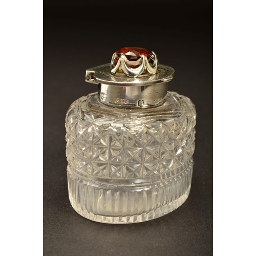 194 - AN EDWARDIAN SILVER MOUNTED OVAL GLASS INKWELL, the hinged cover set with a Cairngorm (brown quartz)... 