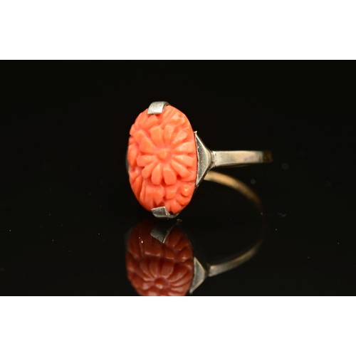 24 - AN EARLY 20TH CENTURY CARVED CORAL RING, an oval floral panel measuring approximately 15mm x 10mm, r... 