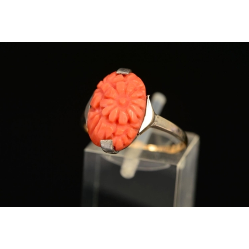 24 - AN EARLY 20TH CENTURY CARVED CORAL RING, an oval floral panel measuring approximately 15mm x 10mm, r... 