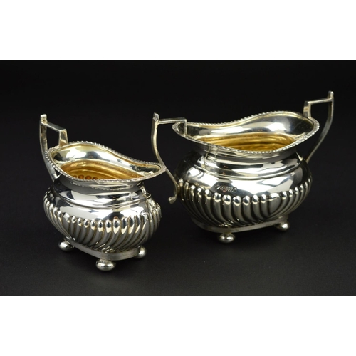 98 - AN EDWARDIAN SILVER OVAL CREAM JUG AND SUGAR BOWL, gadrooned rims and part reeded bodies, on flatten... 