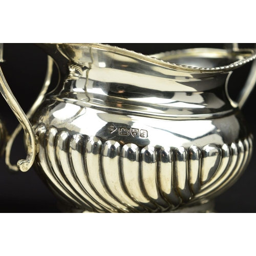 98 - AN EDWARDIAN SILVER OVAL CREAM JUG AND SUGAR BOWL, gadrooned rims and part reeded bodies, on flatten... 