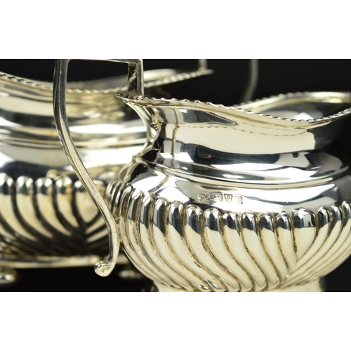 98 - AN EDWARDIAN SILVER OVAL CREAM JUG AND SUGAR BOWL, gadrooned rims and part reeded bodies, on flatten... 