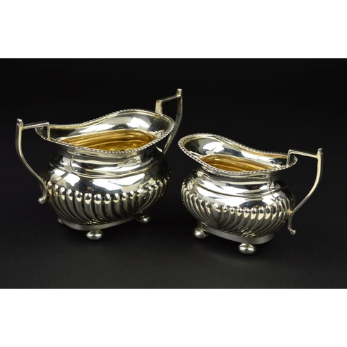 98 - AN EDWARDIAN SILVER OVAL CREAM JUG AND SUGAR BOWL, gadrooned rims and part reeded bodies, on flatten... 