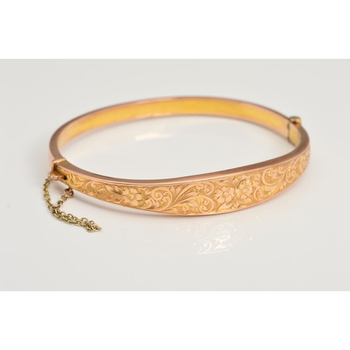 152 - A 1920'S 9CT GOLD HINGED BANGLE, featuring a floral engraved front panel, with a safety chain, with ... 