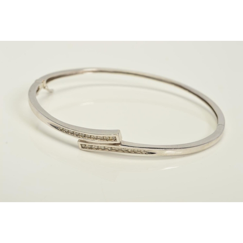 132 - A MODERN 9CT WHITE GOLD DIAMOND HALF HOOP BANGLE, oval in shape cross over design, fitted to a conce... 