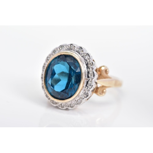 212 - A MODERN 9CT GOLD BLUE TOPAZ AND DIAMOND OVAL CLUSTER RING, centering on an oval dark blue topaz mea... 