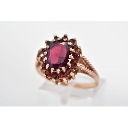 53 - A 9CT GOLD GARNET RING, designed as an oval garnet within a circular garnet surround to the rope twi... 