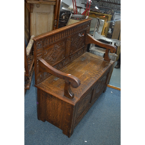 1695 - A REPRODUCTION OAK HALL SETTLE, with four carved panels, hinged storage compartment flanked by open ... 