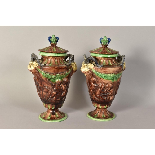 334 - A PAIR OF MAJOLICA URNS AND COVERS, having animal head handles, embossed children at play detailing ... 