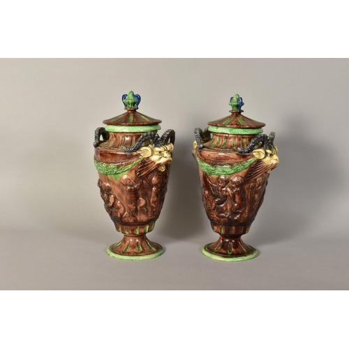 334 - A PAIR OF MAJOLICA URNS AND COVERS, having animal head handles, embossed children at play detailing ... 