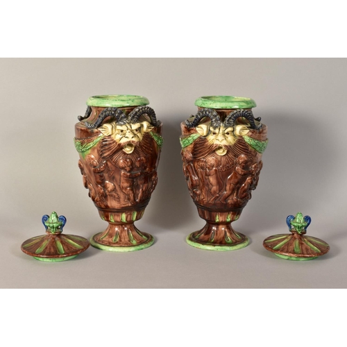 334 - A PAIR OF MAJOLICA URNS AND COVERS, having animal head handles, embossed children at play detailing ... 