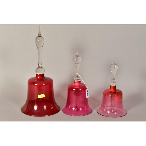 349 - THREE VICTORIAN GLASS BELLS, with cranberry tinted bowls and turned handles, of various heights, tal... 