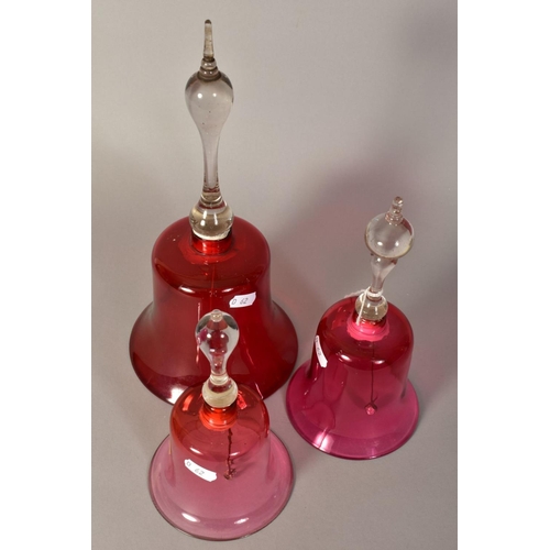 349 - THREE VICTORIAN GLASS BELLS, with cranberry tinted bowls and turned handles, of various heights, tal... 