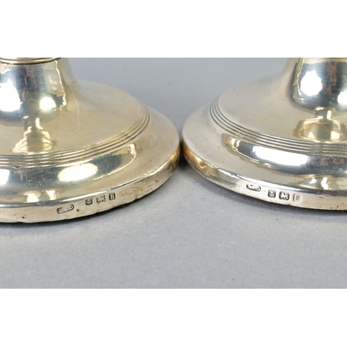 101 - A NEAR PAIR OF EDWARDIAN SILVER CANDLESTICKS, concentric band decoration to rims, inverted conical s... 