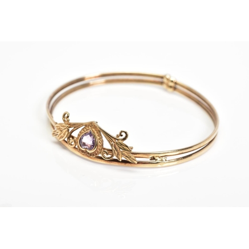 20 - AN AMETHYST BANGLE, designed with a heart shape amethyst in a collet setting within a foliate surrou... 