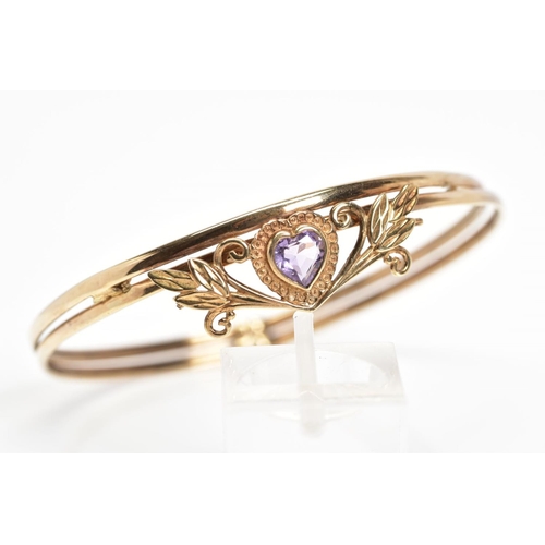 20 - AN AMETHYST BANGLE, designed with a heart shape amethyst in a collet setting within a foliate surrou... 