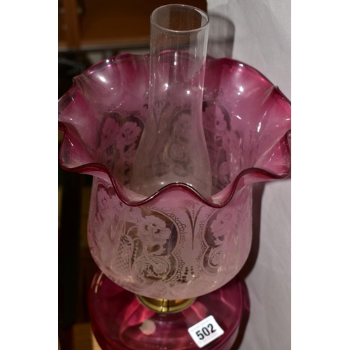 502 - A LATE VICTORIAN CRANBERRY GLASS AND BRASS OIL LAMP, the wavy rimmed shade acid etched with floral d... 